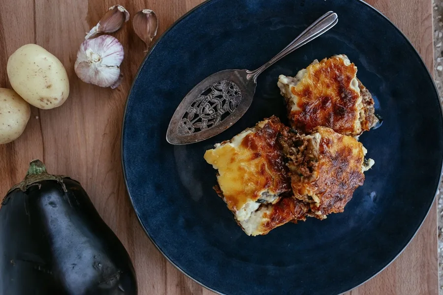 Porción de musaka griega tradicional servida en plato azul con berenjena fresca